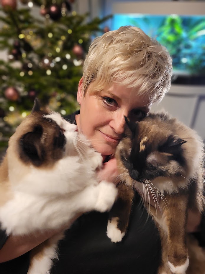 Katja Schneider mit zwei Katzen vor einem festlichen Baum.
